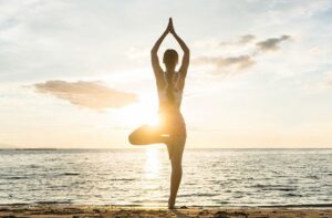 Femme en posture de l'Arbre (Vrksasana) en bord de mer au coucher du soleil, symbole de l'équilibre pour la méditation au Pradet.
