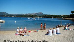 Groupe de vacanciers assis sur la plage du Pradet avec vue sur les collines et les bateaux en Méditerranée.
