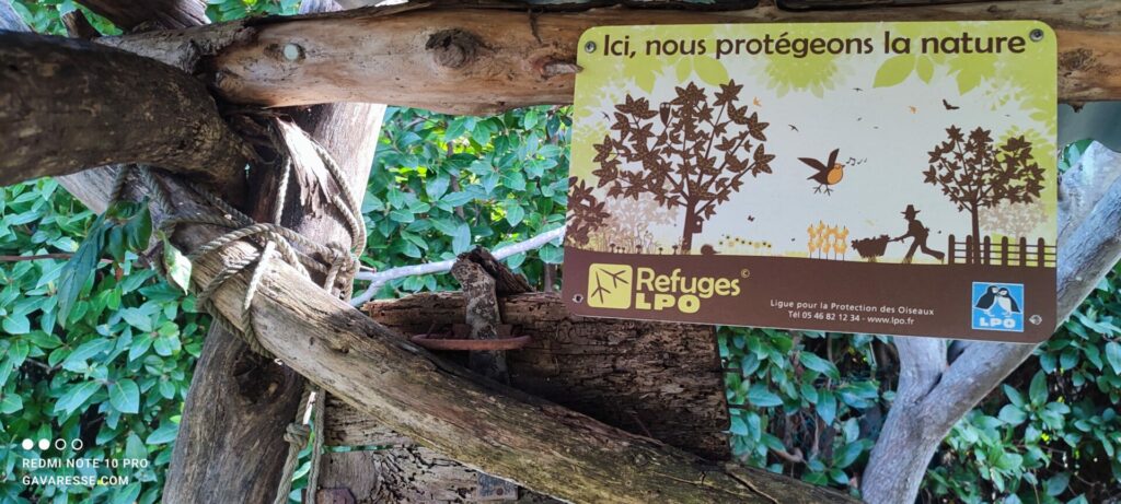 Plaque "Ici, nous protégeons la nature" des Refuges LPO fixée sur une structure en bois au Mas Gavaresse.