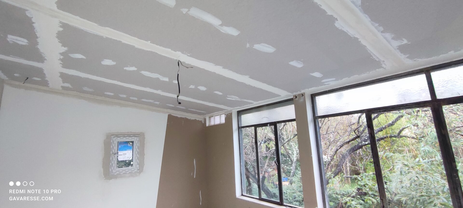 Application des bandes à joints sur les plaques de plâtre du nouveau plafond. Le nouveau fenestron blanc et la verrière historique sont visibles en arrière-plan.