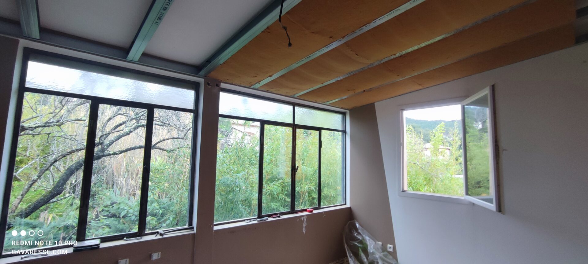 Installation de panneaux de laine de bois entre les rails métalliques du plafond suspendu. La verrière historique et une fenêtre ouverte sont visibles en arrière-plan.