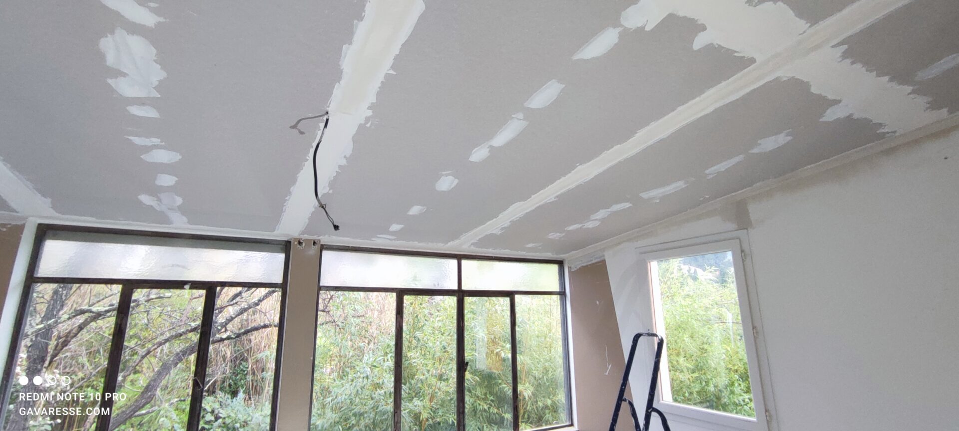 Nouveau plafond en plaques de plâtre posé sur l'isolation en laine de bois. Les bandes de jointoiement blanches sont visibles sur les plaques grises au-dessus de la verrière.