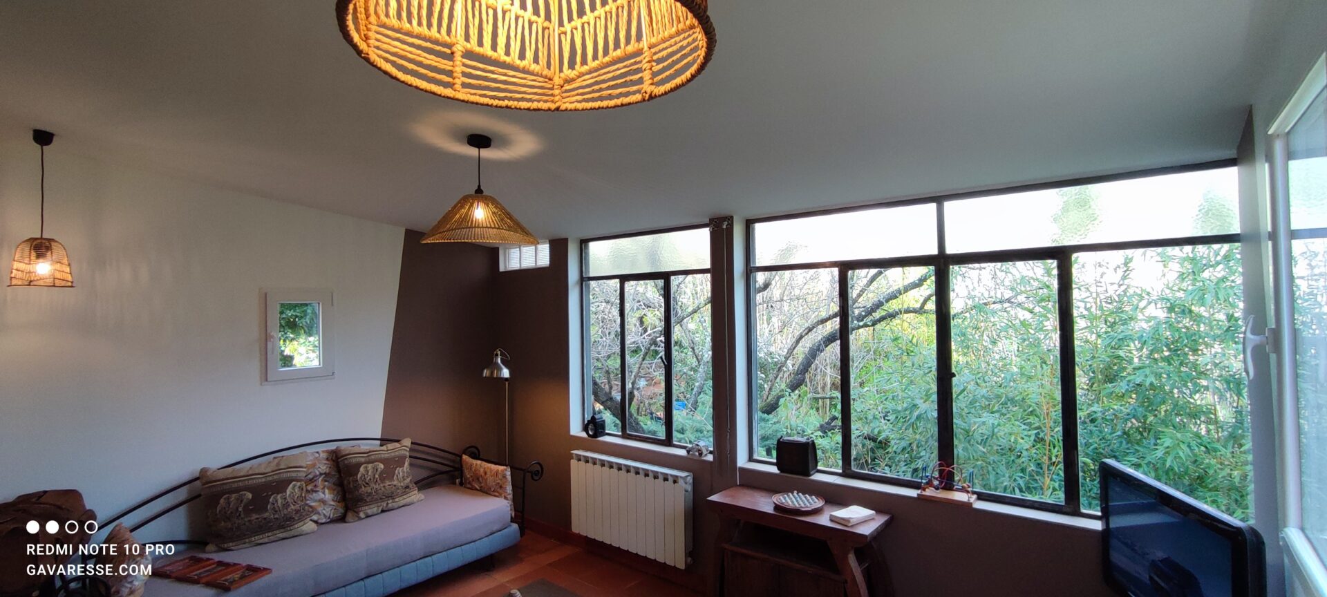 Salon du gîte l'Orangeraie au Pradet avec éclairage d'ambiance, suspensions en osier, banquette en fer forgé et vue sur le jardin de bambous.