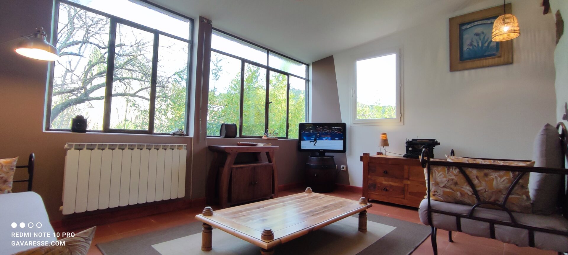 Salon lumineux du gîte l'Orangeraie au Pradet avec grande verrière en fer, table basse en bois massif et sol en terre cuite.